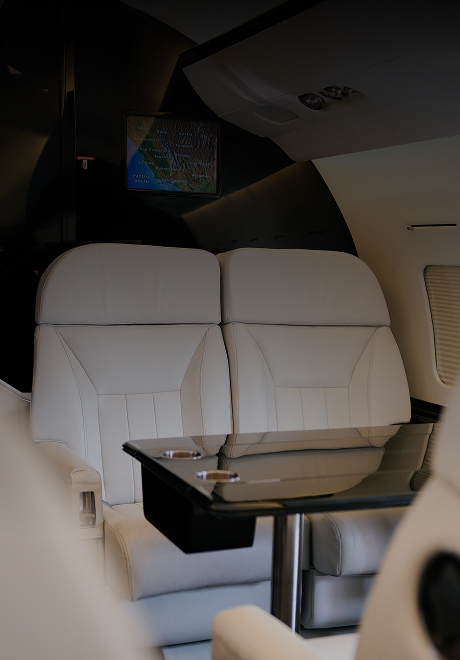 Challenger 604 private jet interior featuring two white leather seats, a black glass table, and in-flight map screen.