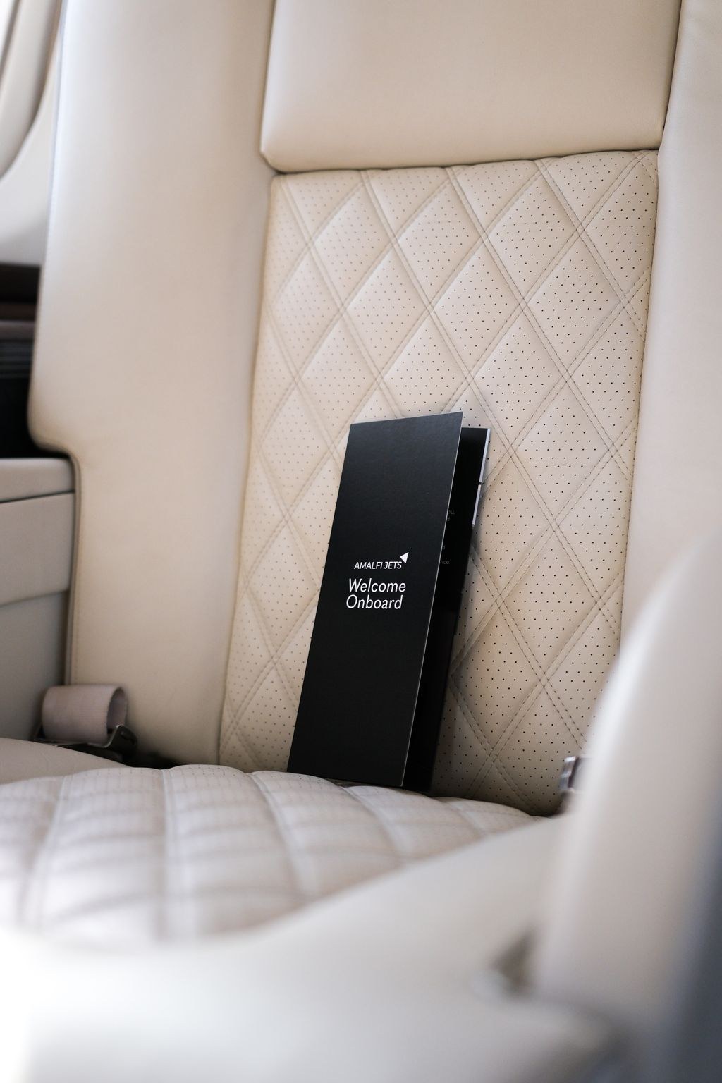 Quilted cream leather seat in a private jet cabin with a Welcome Onboard card resting on it.