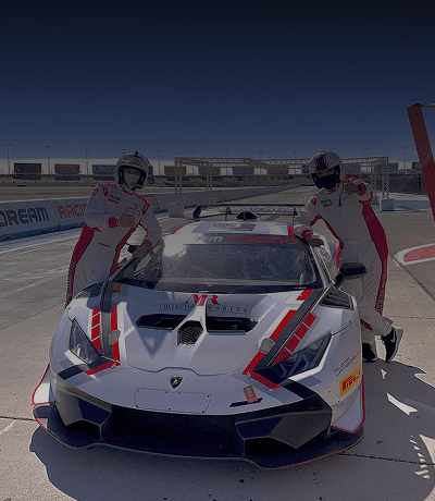 Two men in racing uniforms posing with a white and red Lamborghini racecar at Dream Racing Las Vegas.