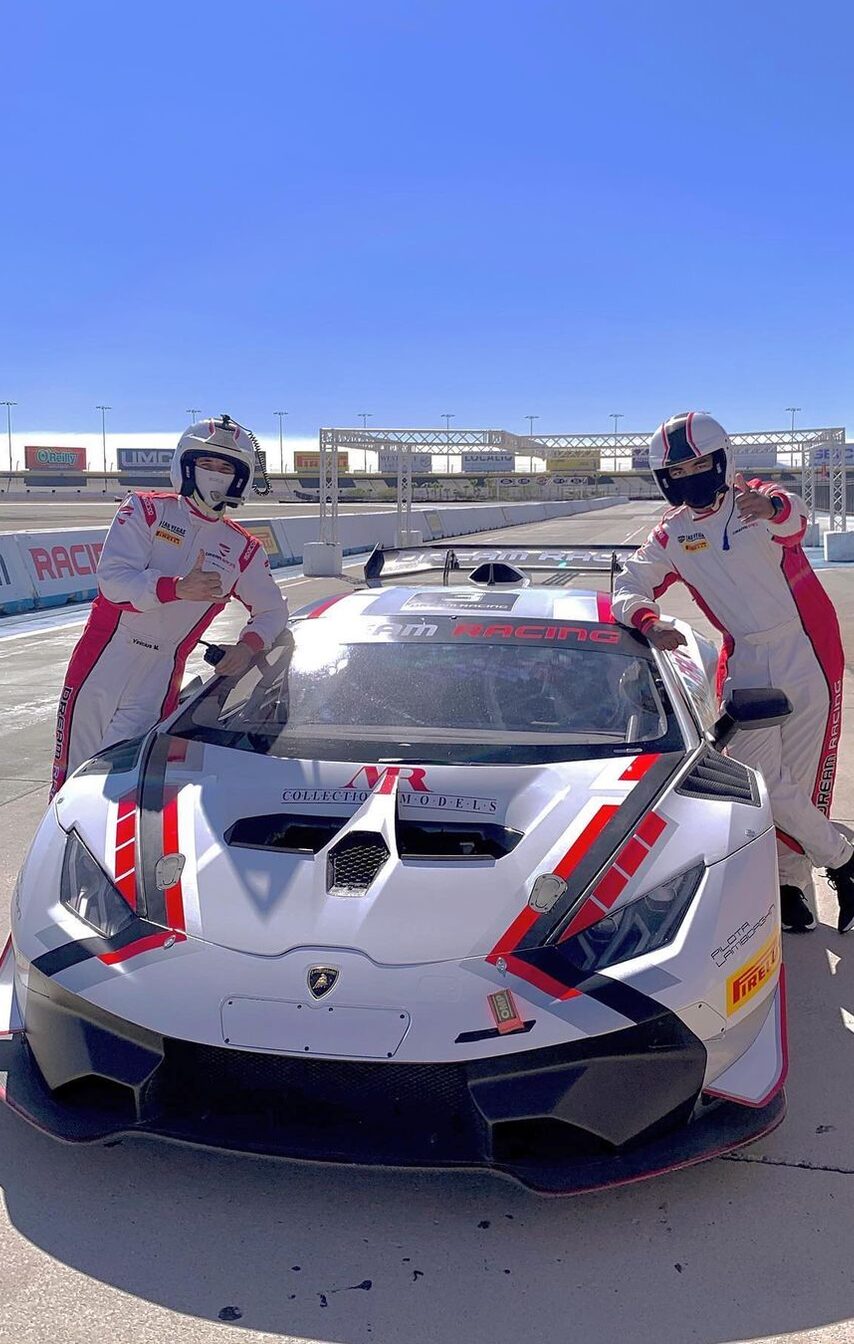 Two drivers in racing suits standing beside a Lamborghini race car at the speedway.