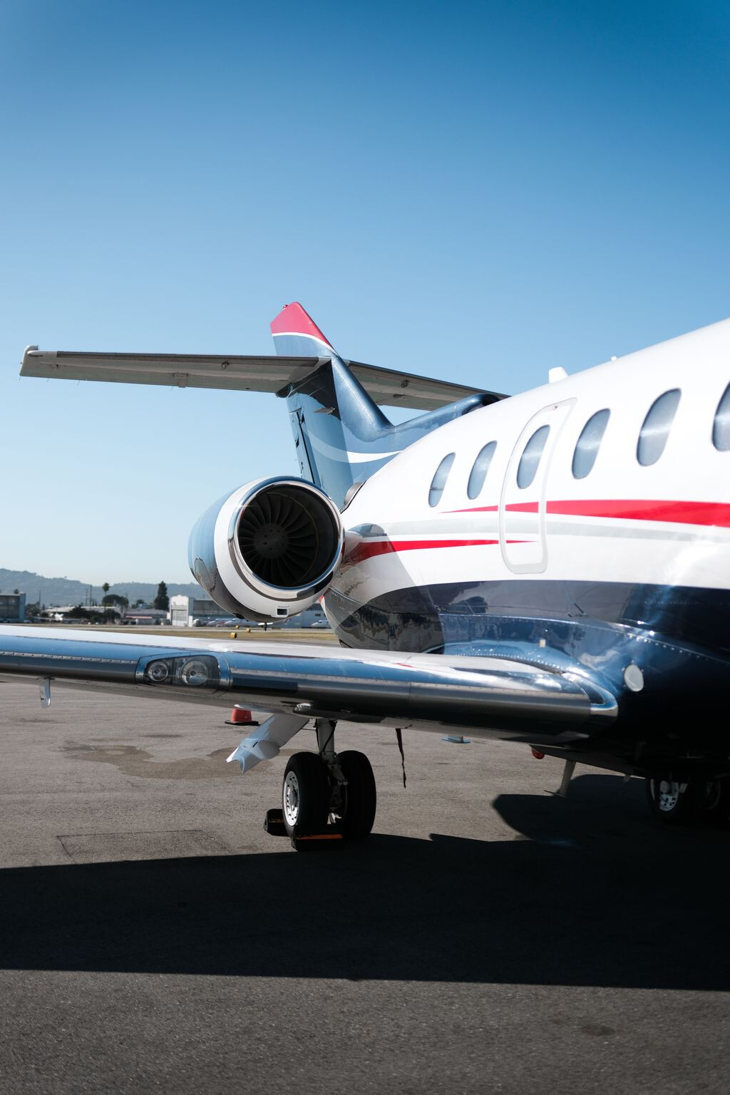 Rear quarter of a red, white, and blue private jet beneath a clear sky.