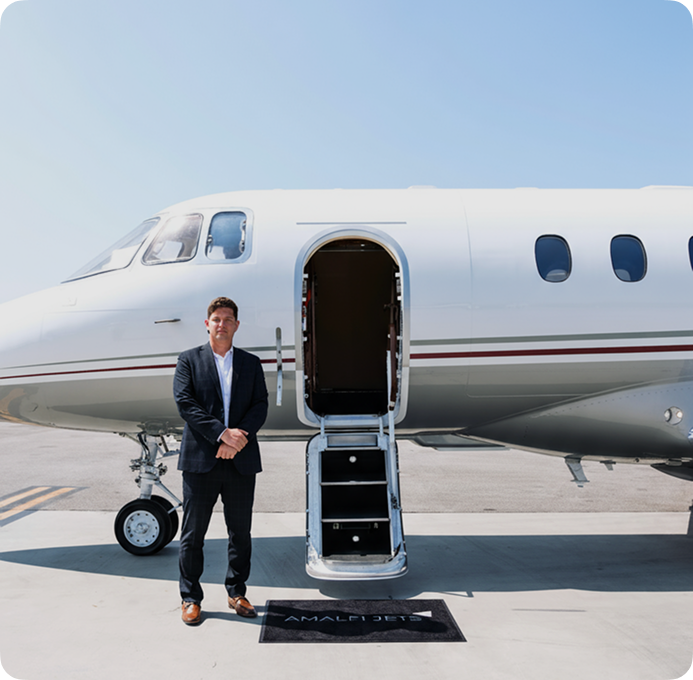 Amalfi Jets President of Operations standing beside a Hawker 900XP private jet with the cabin door open on the tarmac.