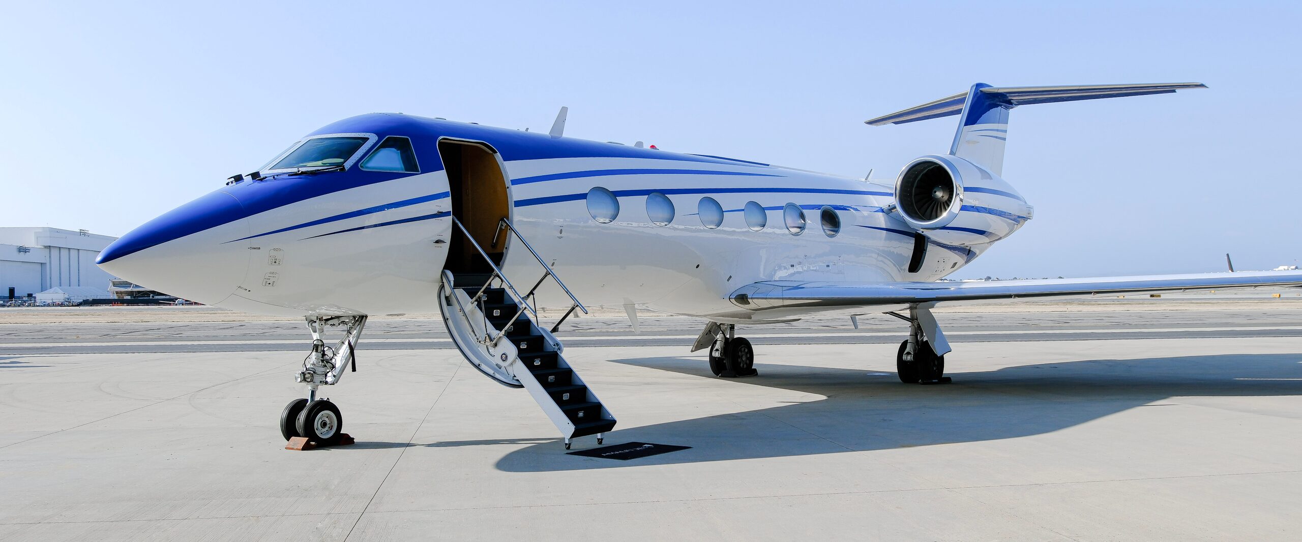 Blue and white Gulfstream private jet parked on the tarmac with its airstair door lowered.