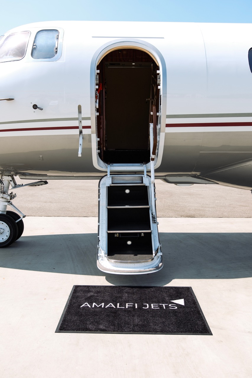 Elegant Hawker 900 midsize jet on tarmac with open cabin door and Amalfi Jets mat at the entryway.
