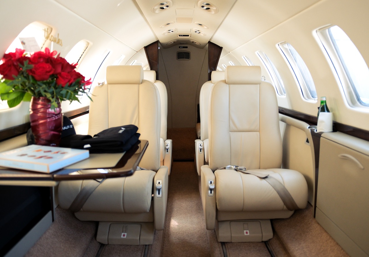 Cessna Citation CJ3 cabin interior featuring beige leather seats, fold-out tables, and bright natural lighting.