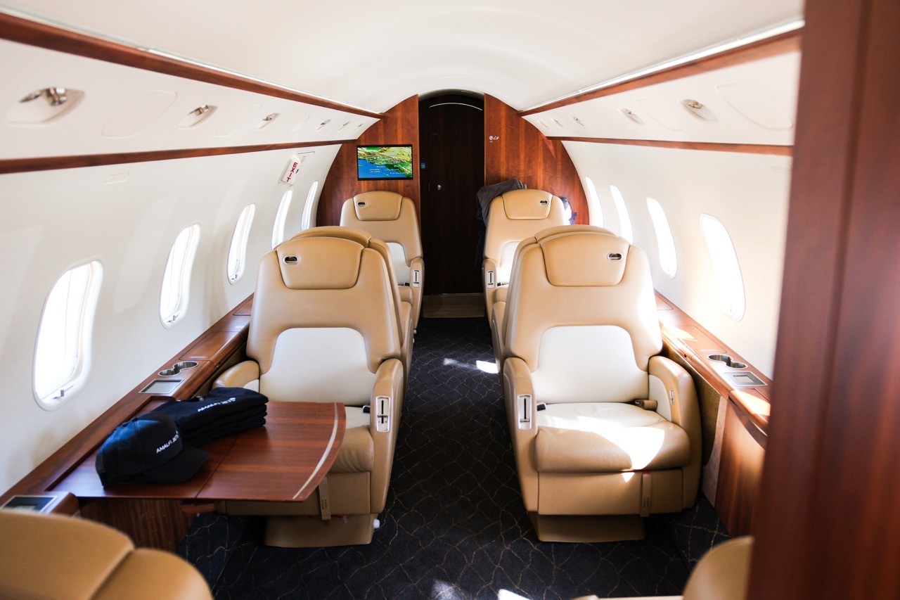 Luxurious Challenger 300 cabin with tan leather seats, wooden finishes, and widescreen inflight display.
