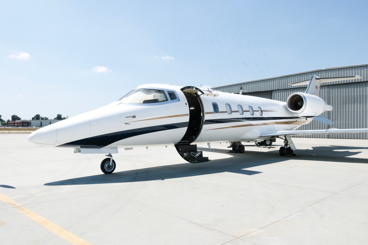 Wide length image of Learjet 60 on tarmac with open cabin door and swept-wing design.