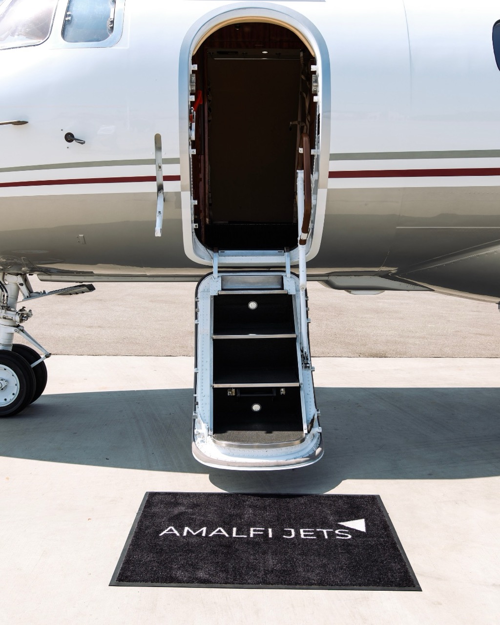 Amalfi jets branded black rug layed out in front of a hawker 900 xp passenger entry door.