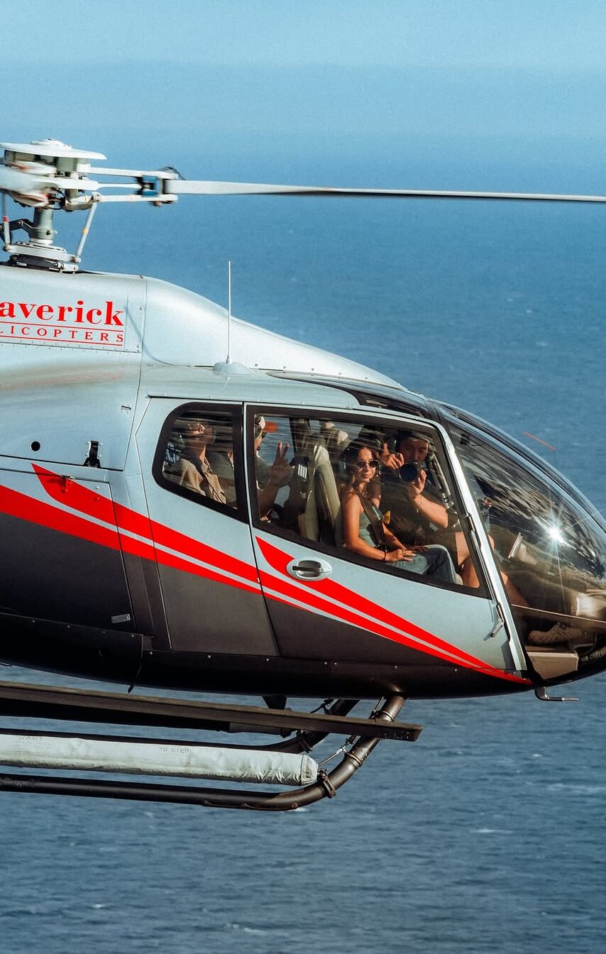Passengers seated inside a Maverick helicopter cabin above the coastline.