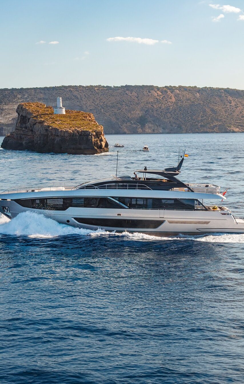 A white superyacht cruising past a rocky headland at sunset.