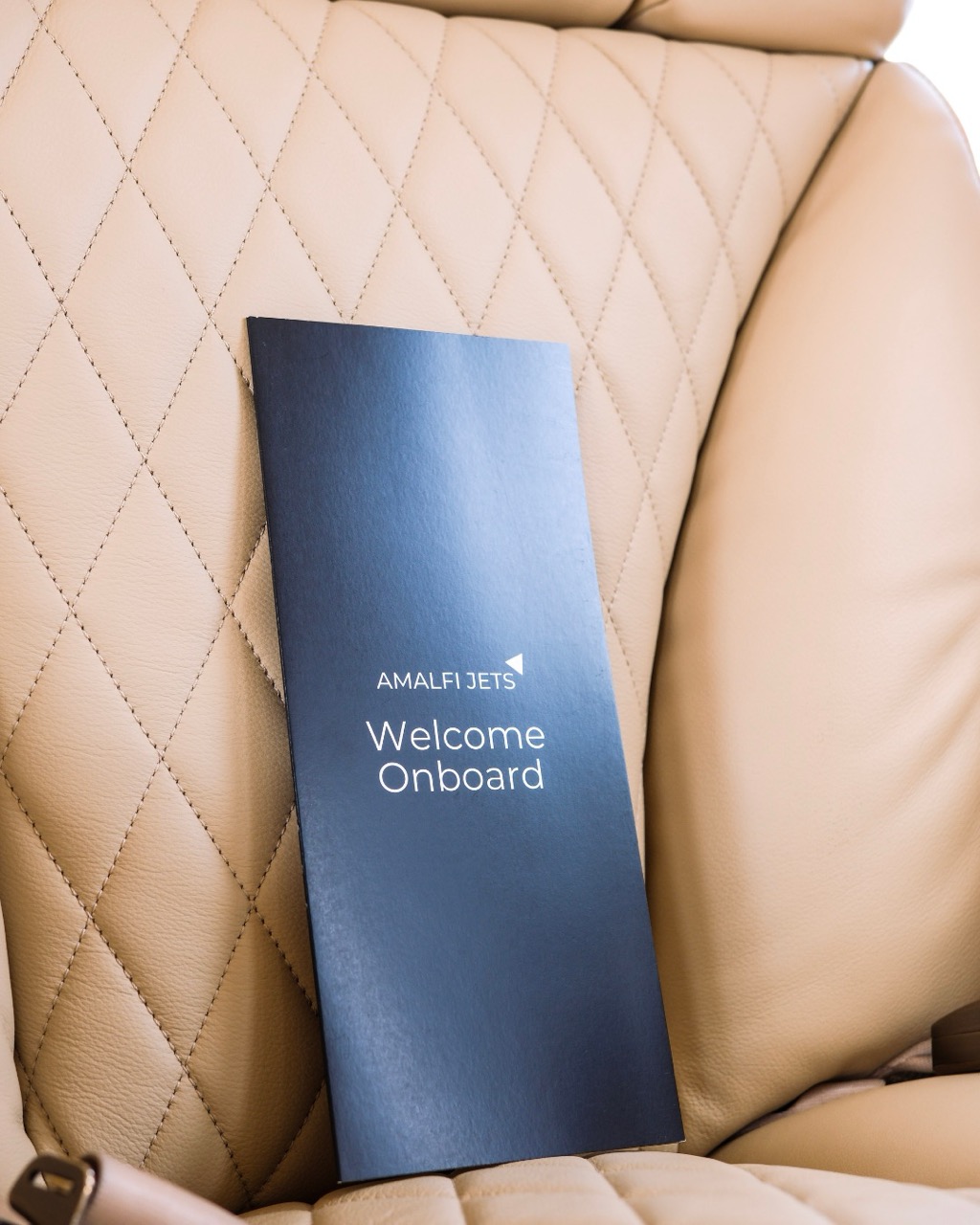 Amalfi jets welcome onboard black brochure sitting on a tan private jet seat.