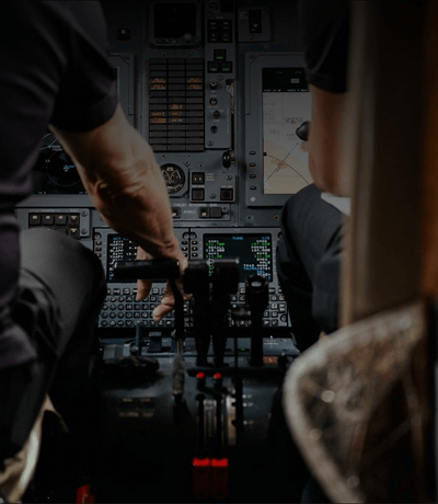 Private jet cockpit interior with two pilots seated, hands on controls and illuminated flight instruments.